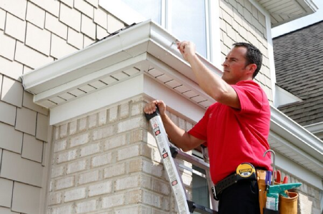 Handyman standing on ladder inspecting gutter