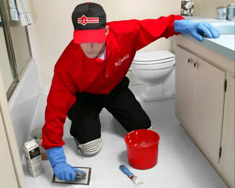 A handyman from Mr. Handyman using a trowel to spread tile cleaner over a newly installed tile bathroom floor.