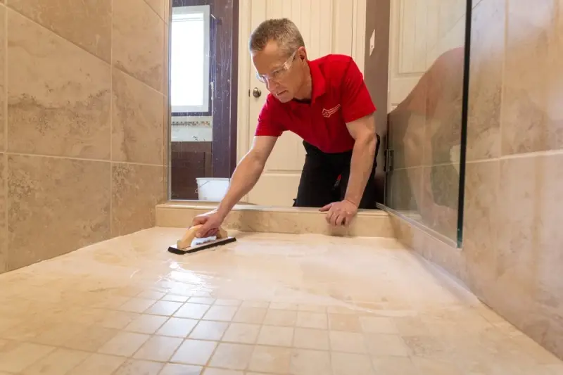 A handyman from Mr. Handyman using a trowel to spread tile cleaner across the tile floor of a shower.