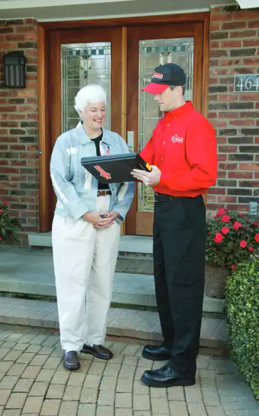 Mr. Handyman aging-in-place specialist with older homeowner in front of home looking at clipboard.