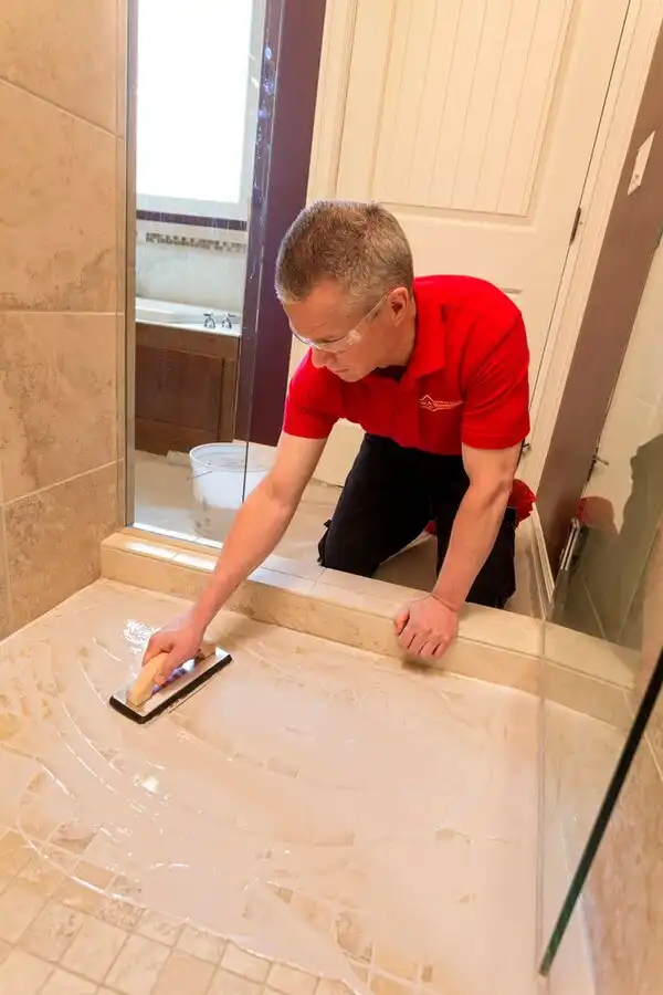 A handyman from Mr. Handyman using a trowel to spread grout haze remover over newly installed shower floor tiles.