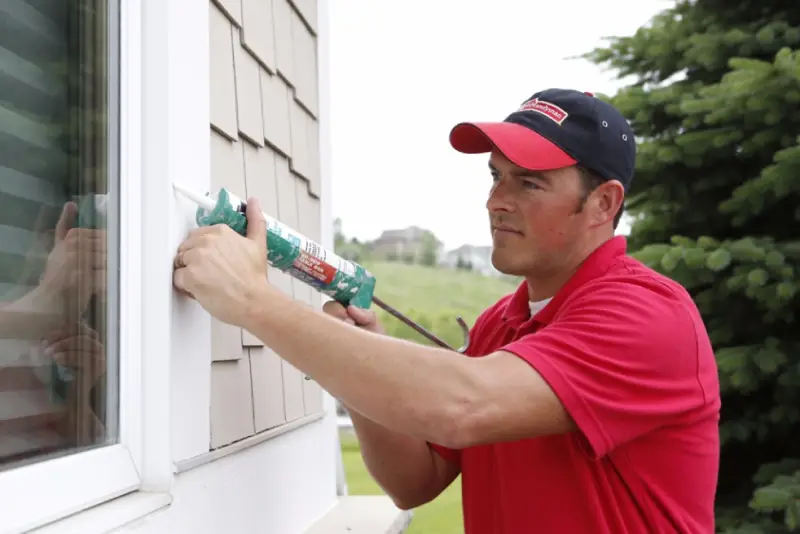 A handyman fixing the seal around the outside of a window in need of window repair in Charleston, SC.