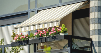 An awning extended over flowers on the balcony of a home that has just received awning installation service.