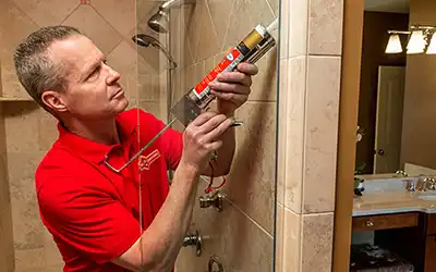 A Mr. Handyman repairman caulking a Spokane, WA home's bathroom shower.