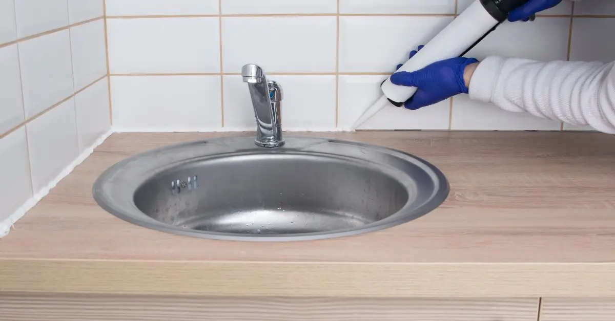 A technician caulking a gap between a tile wall and a countertop behind a sink in a bathroom during an appointment for caulking service in Charleston, SC.