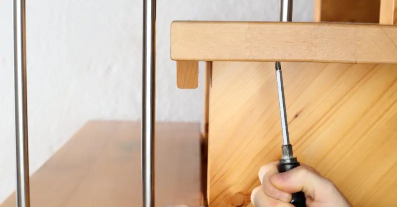 A handyman using a screwdriver to repair the railing on a staircase during an appointment for stair repair in Frisco, TX.