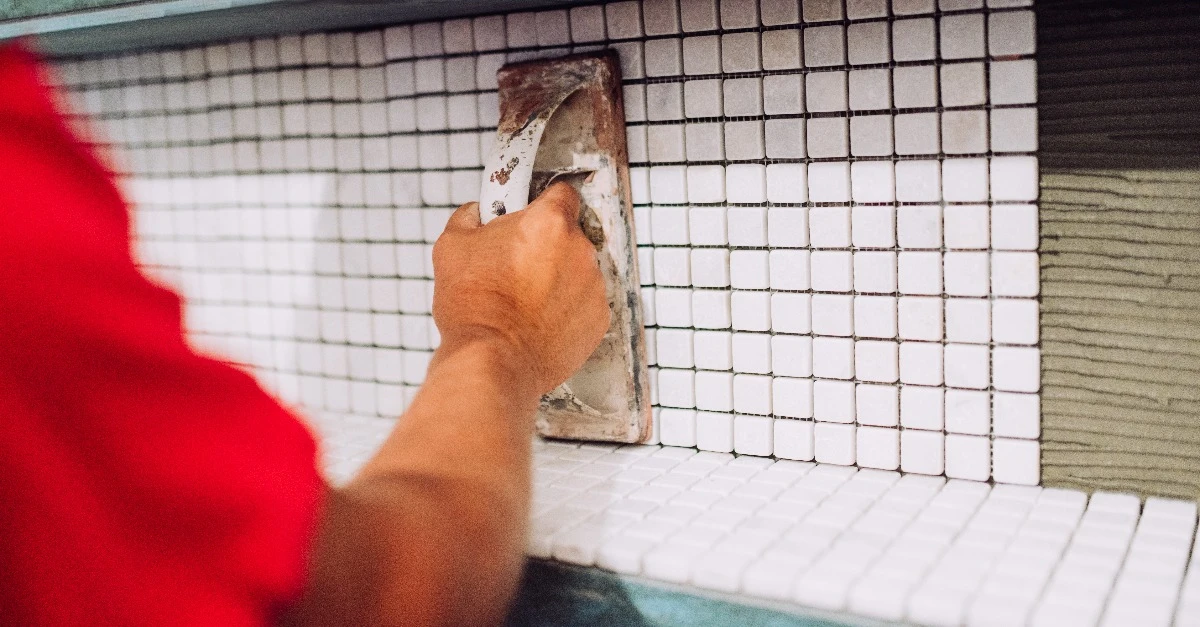 A handyman using a flat trowel to level out an area of new tiles installed on a backsplash during an appointment for tile repair in Frisco, TX.A handyman using a flat trowel to level out an area of new tiles installed on a backsplash during an appointment for tile repair in Frisco, TX.