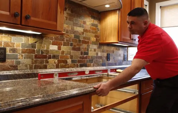 A handyman from Mr. Handyman using a level to inspect a new kitchen countertop installed during a kitchen remodel in Naples, FL.