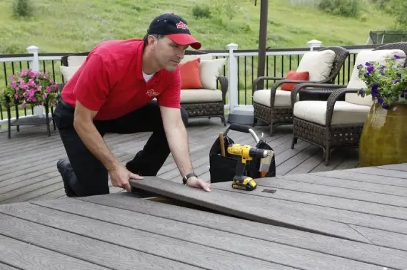 A handyman from Mr. Handyman placing a new deck board into an existing deck during an appointment for deck repairs.