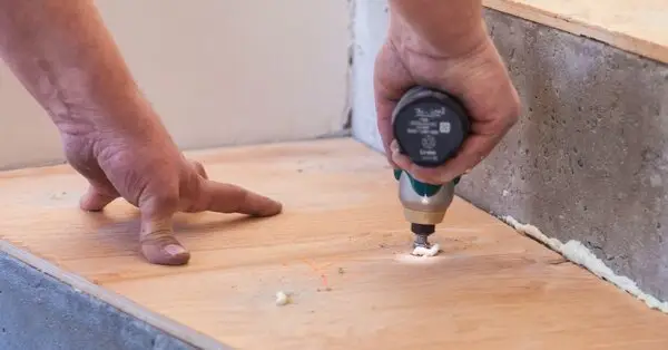 A handyman using a small power drill to attach a wooden board on top of a set of concrete steps during an appointment for stair repair in Walpole, MA.