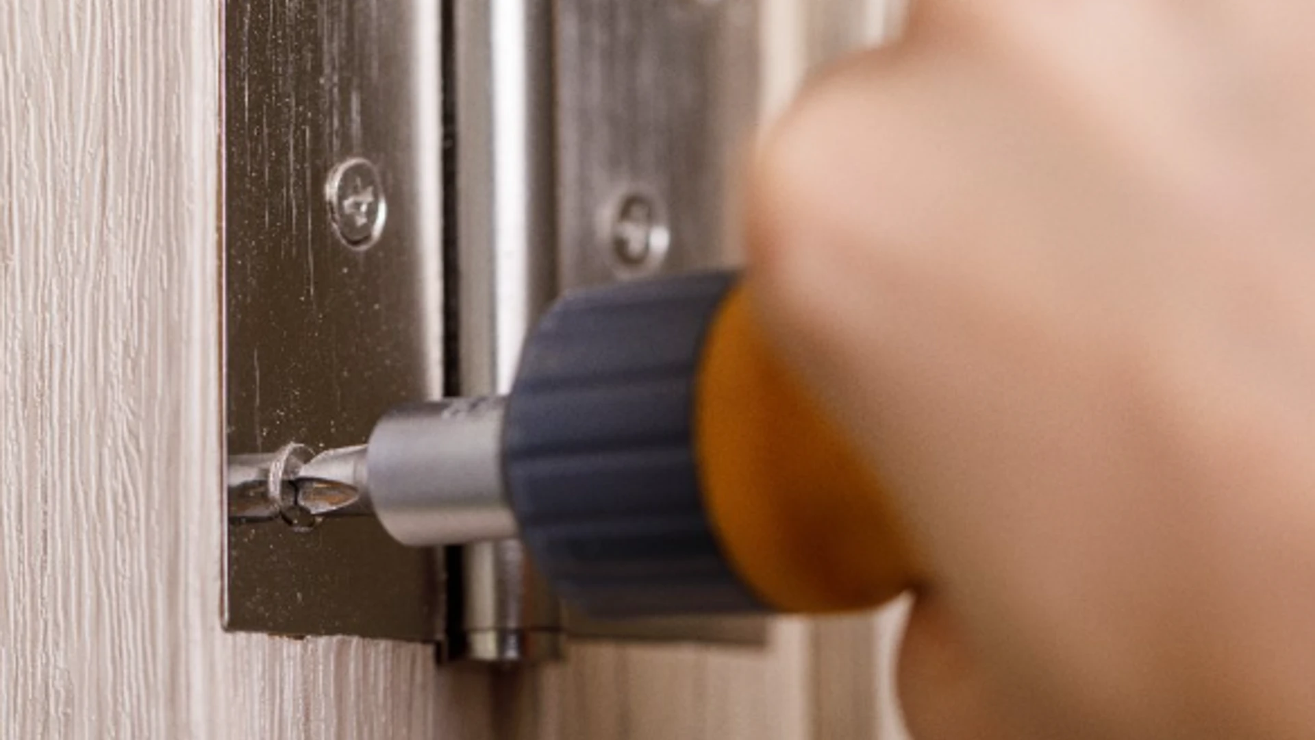 A handyman using a screwdriver to attach new hinges to an interior door frame during an appointment for interior door repair in frisco, TX.