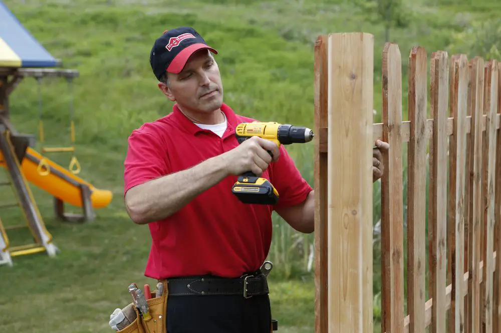 A handyman replacing fence posts on a wooden fence while providing services for carpentry in Charleston, SC.