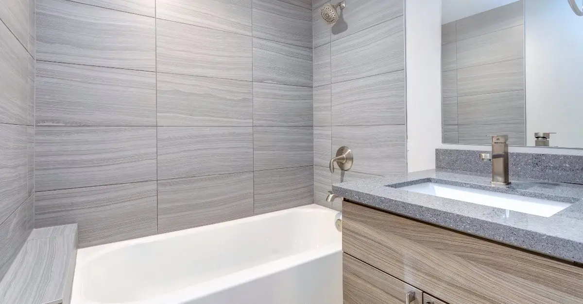 A newly completed bathroom remodel with new gray shower tiles, a speckled gray countertop, and a built-in shower bench.