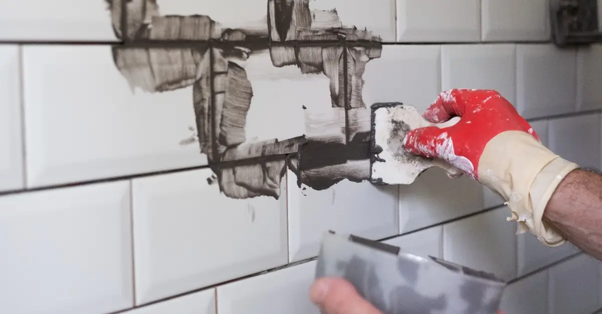 A hand holding a putty knife and spreading grout sealer over a tiled surface that has just received grout repairs in Dallas, TX.