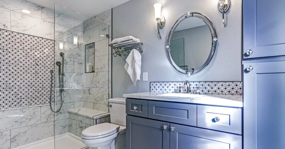 A newly remodeled bathroom with light-blue cabinets, white marble shower tiles and a glass shower enclosure.