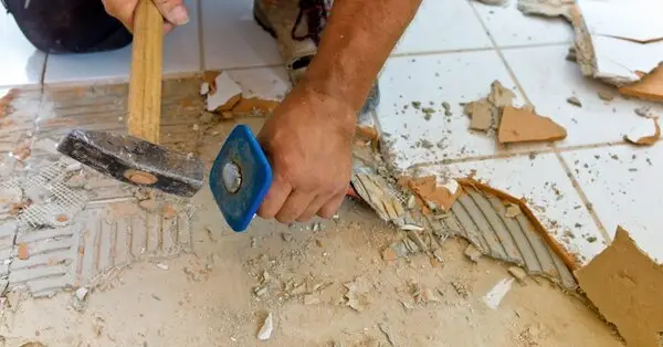 A handyman using a chisel to remove damaged tiles during an appointment for tile repair in Vancouver, WA.