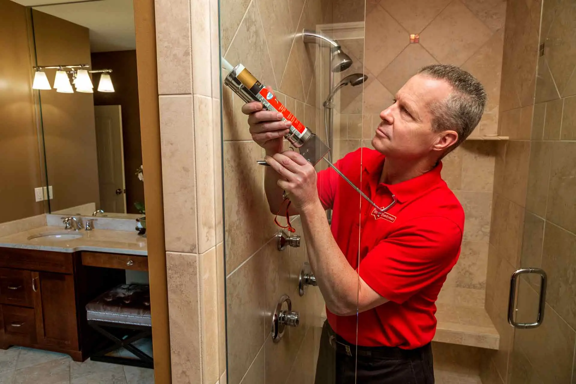 A handyman from Mr. Handyman using a caulking gun to seal the glass wall of a shower during a small bathroom remodel Vancouver, WA.