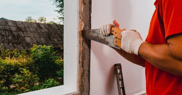 A handyman using a saw to loosen and remove part of a window frame during an appointment for window repair in Knoxville, TN.