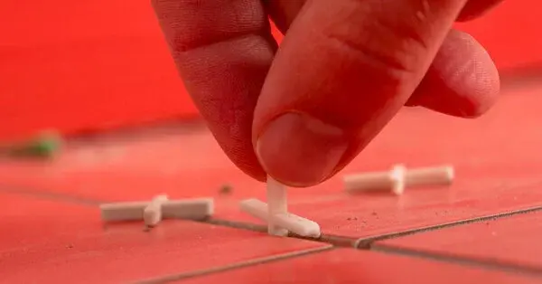 A close-up of a person’s fingers as they insert tile spacers between red tiles to leave space for grout during a tile installation project.