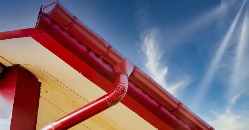 Red, half-circle shaped gutters and a red downspout attached to a home’s roof after an appointment for gutter installation.