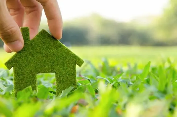 A hand holding a grass house in the grass.