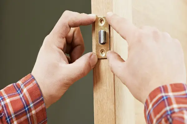 A handyman installing the faceplate for a door latch while performing door repairs in Frisco.