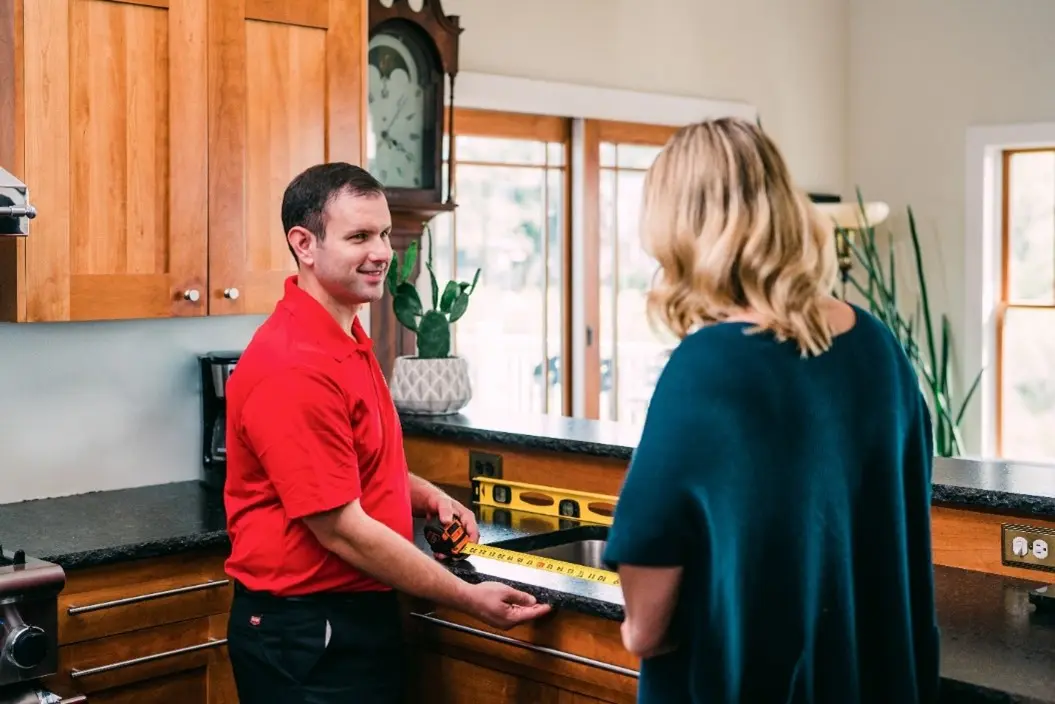 A Mr. Handyman technician speaking with a client while measuring a kitchen sink.