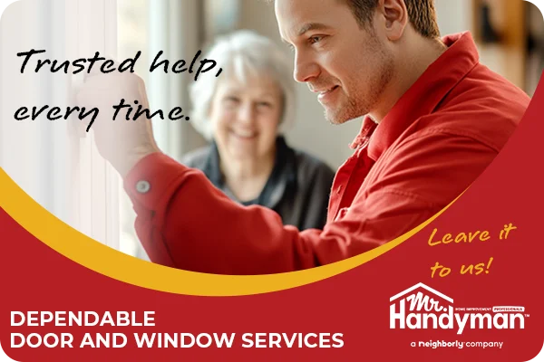 Handyman in red uniform fixing a door as a smiling senior lady looks on.