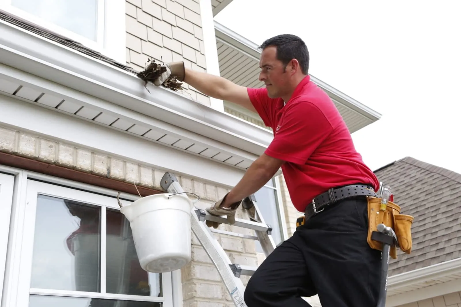 A handyman from Mr. Handyman standing on a ladder while providing services for gutter cleaning in Dallas, TX