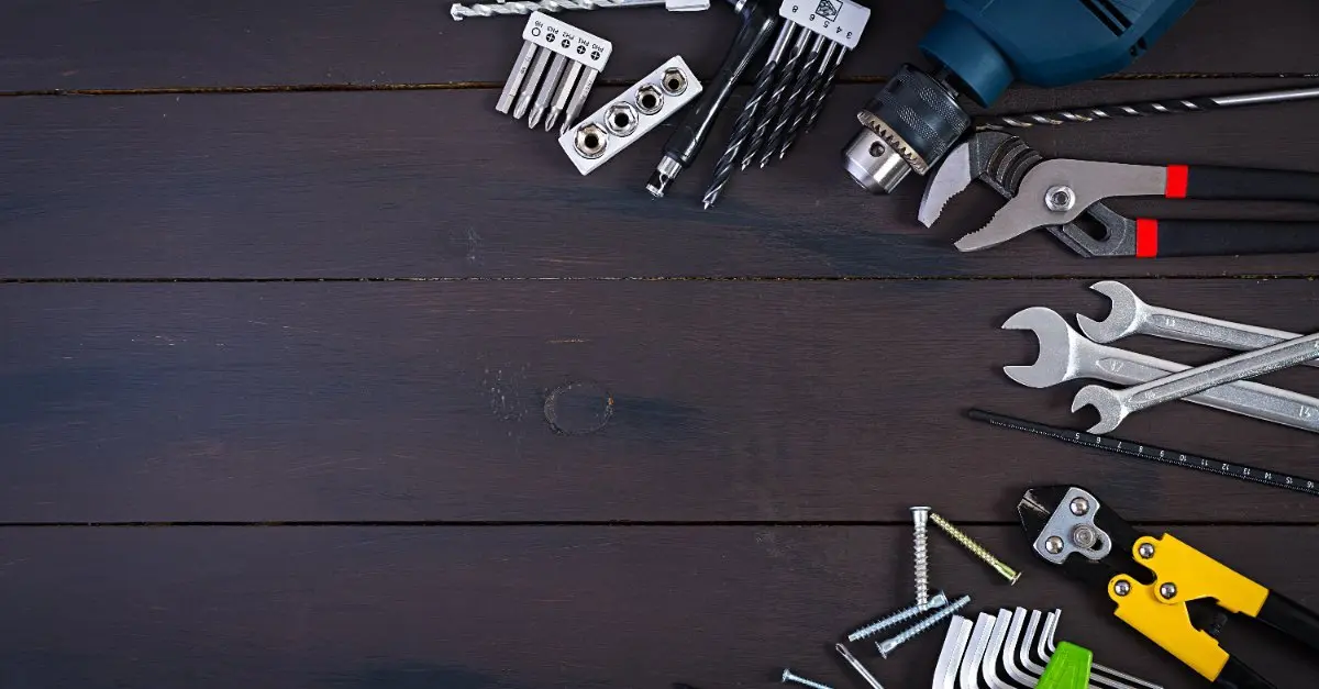 A dark, wooden background with a collection of tools that could be used for NoVA commercial handyman service, including a power drill, pliers, and wrenches of various sizes.