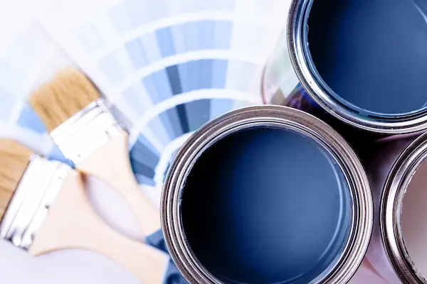 Paintbrushes and a color wheel beside blue paint cans.